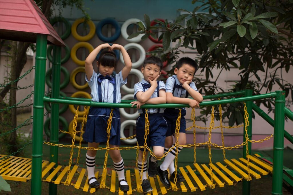pexels photo 35128479 Three children in uniform having fun on a vibrant playground bridge outdoors.